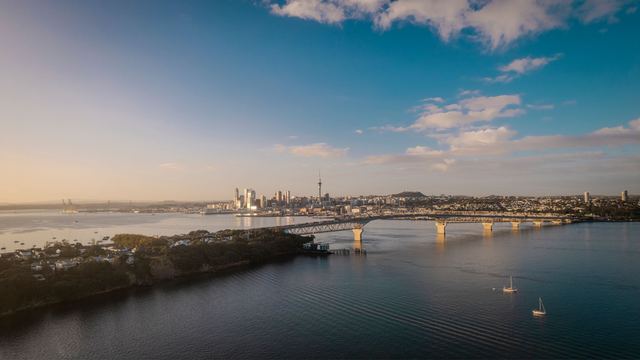 Aerial view of the Auckland city skyline and Sky Tower with the Harbour Bridge over Waitematā Harbour at sunset.