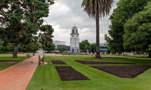 The stone war memorial clock tower in Seymour Square, Blenheim, beyond lawns and garden beds.