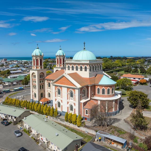 Aerial view of Timaru's Sacred Heart Basilica with its copper domes, the town and the sea behind.