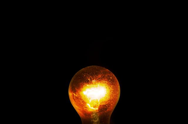 A dusty incandescent light bulb glowing orange against a black background.