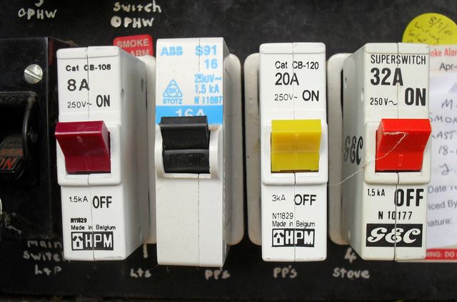 Four old circuit breakers in an Australian meter box, with hand-written circuit labels for lights, power points and stove underneath.