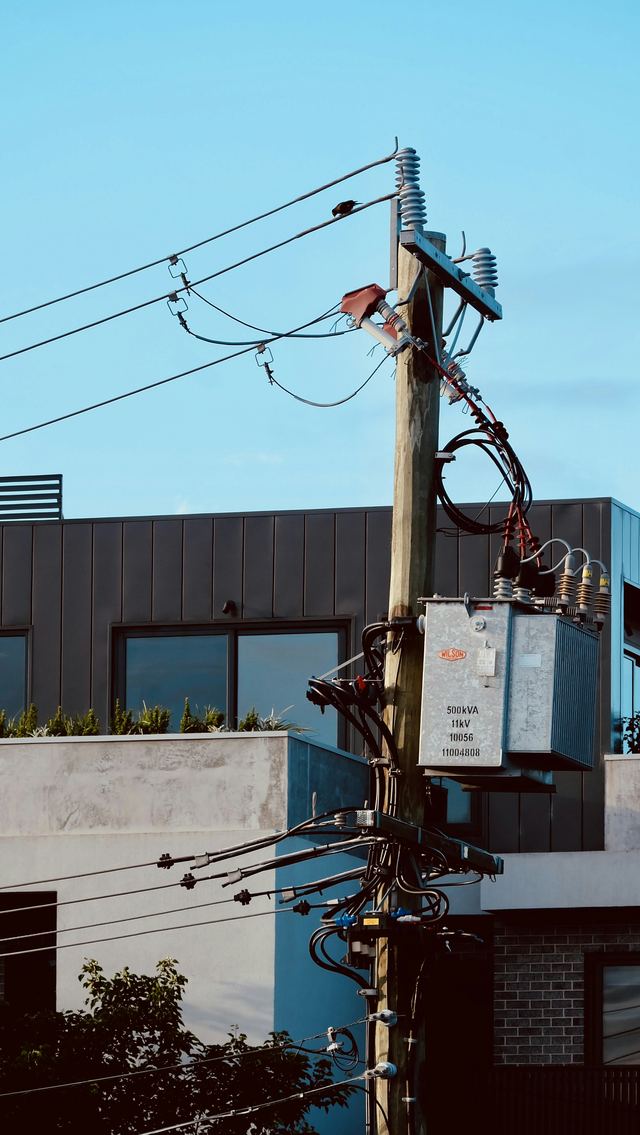 A timber power pole carrying a pole-mounted transformer and black overhead service cables in front of modern townhouses.