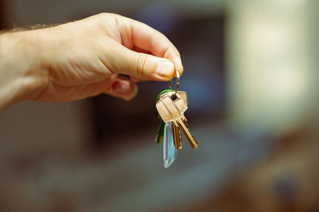 A hand holding up a small bunch of house keys on a ring against a blurred room.
