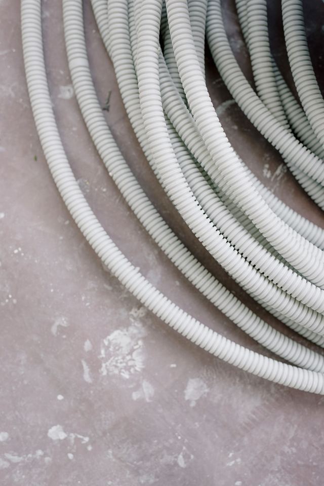 Coils of grey flexible electrical conduit lying on a dusty concrete floor.